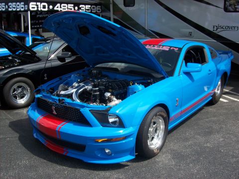 2007 Ford Mustang - A bright blue 2007 Ford Mustang with racing stripes is displayed with its hood open, next to another Mustang.