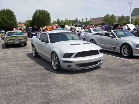 2007 Ford Mustang - A silver Ford Mustang is parked in a lot with other vehicles and people.