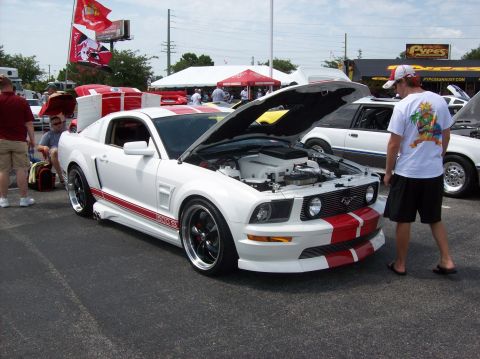 2007 Ford Mustang - A white 2007 Ford Mustang with red racing stripes is displayed with its hood open at an outdoor event.