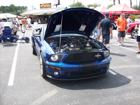 2007 Ford Mustang - A blue Ford Mustang is parked with its hood up, revealing the engine compartment. People are visible in the background.