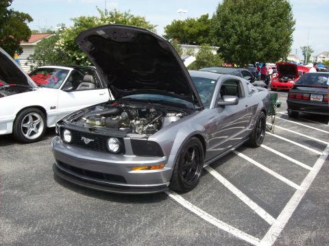 2007 Ford Mustang - A gray 2007 Ford Mustang is displayed with its hood open at an outdoor car event, alongside other vehicles.