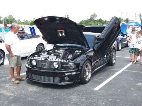2007 Ford Mustang - A man looks at a black Ford Mustang with custom doors open at a car show.