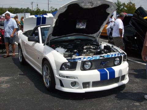 2007 Ford Mustang - A white convertible Ford Mustang with blue racing stripes is displayed with its hood open, revealing the engine bay.