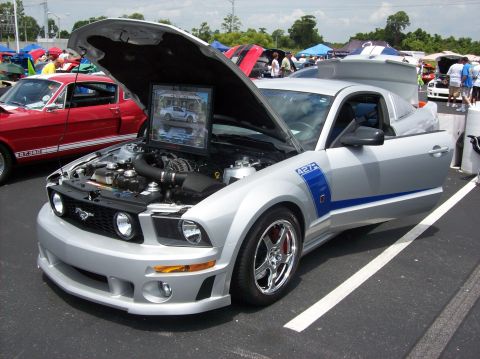 2007 Ford Mustang - A silver 2007 Ford Mustang is displayed with its hood open, a blue stripe and a framed photo on the engine.