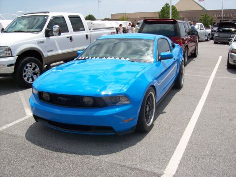 2007 Ford Mustang - A bright blue coupe is parked in a lot next to a white pickup truck. The car has black rims and appears to be a 2010 model.