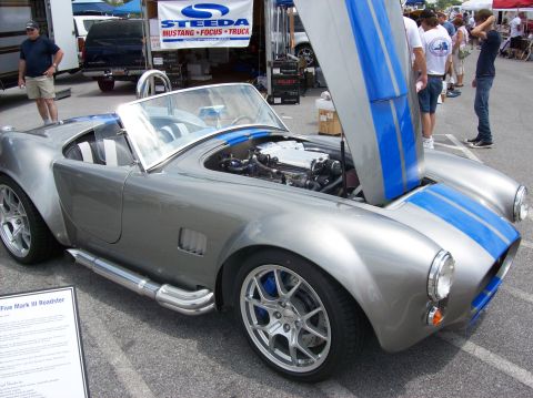 2007 Ford Mustang - Silver Shelby Cobra replica with blue racing stripes and exposed engine at an outdoor event.