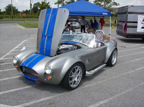 2007 Ford Mustang - A silver Shelby Cobra replica with blue racing stripes is parked with its hood open.