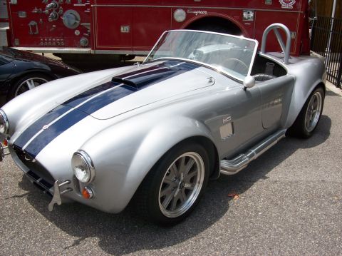 2007 Ford Mustang - A silver convertible sports car with blue racing stripes is parked in front of a red fire truck.