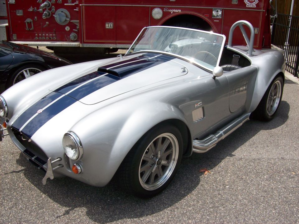 Silver convertible sports car with dual blue racing stripes and side exhaust pipes