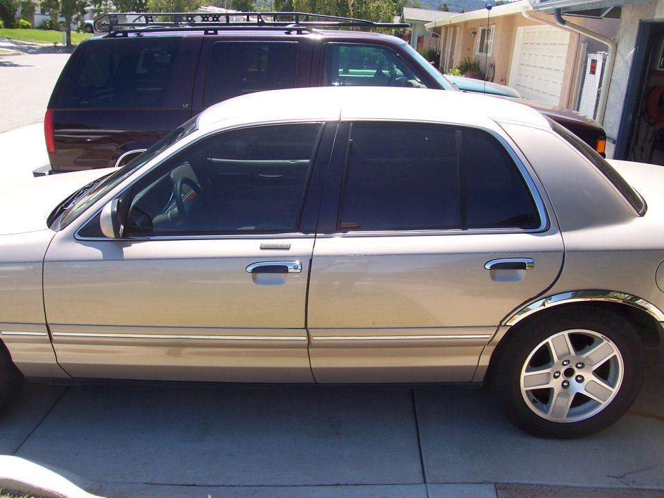 Tan four-door sedan side profile with alloy wheel parked in a driveway near an SUV