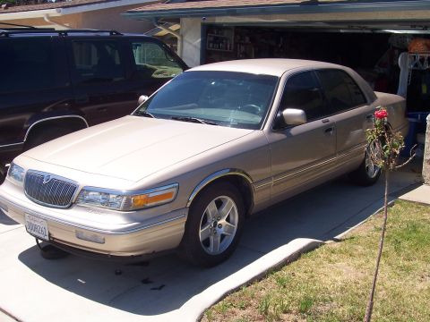 1997 Mercury Grand Marquis - A tan 1997 Mercury Grand Marquis sedan is parked in a driveway next to a dark SUV.