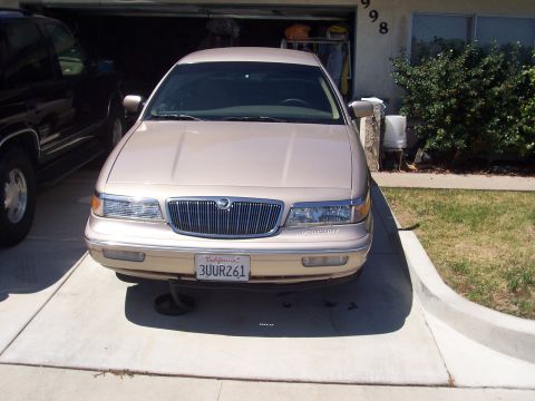 1997 Mercury Grand Marquis - A 1997 Mercury Grand Marquis is parked in front of a garage, showing its front grille and headlights.