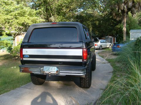1992 Ford Bronco - Rear view of a black 1992 Ford Bronco parked in a driveway with other vehicles visible.