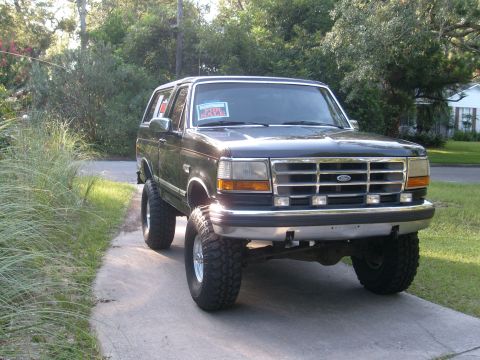 1992 Ford Bronco - A black 1992 Ford Bronco is shown from a three-quarter front view, lifted with large tires.