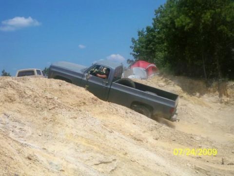 1980 Ford Bronco - A gray pickup truck is seen off-roading on a dirt hill, with another vehicle partially visible in the background.