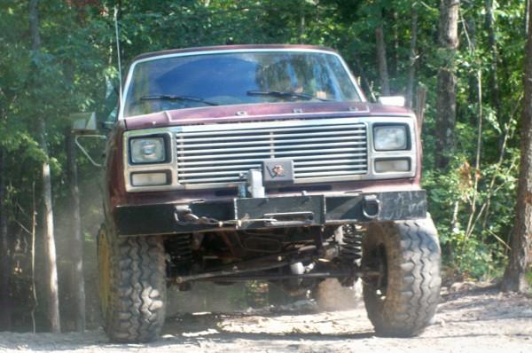 Front view of a lifted, maroon Ford F-Series truck with a large grille and winch