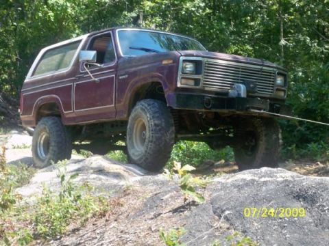1980 Ford Bronco - A maroon 1980 Ford Bronco navigates rocky terrain with off-road tires and a winch.