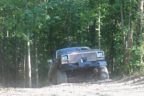 Maroon off-road truck with a large chrome grille, seen from a 3/4 front angle on a dirt path