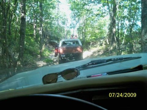 1980 Ford Bronco - Two SUVs navigate a wooded trail on a sunny day, with sunglasses resting on the dashboard.