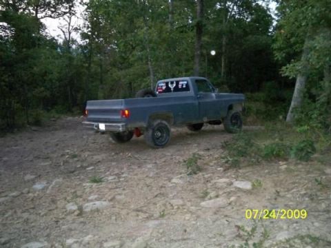 1980 Ford Bronco - A dark blue pickup truck is parked on a dirt road surrounded by trees.