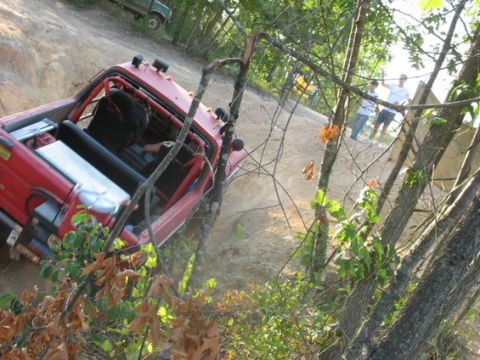 1979 Ford Bronco - A red off-road vehicle is seen navigating a challenging dirt trail, with another vehicle visible in the background.