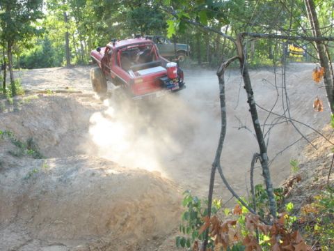 1979 Ford Bronco - Red 1979 Ford Bronco navigates a dusty off-road course, with another vehicle in the background.