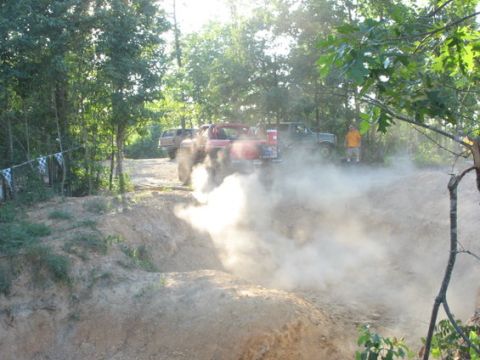1979 Ford Bronco - Multiple trucks are seen off-roading and creating dust clouds in a wooded area.