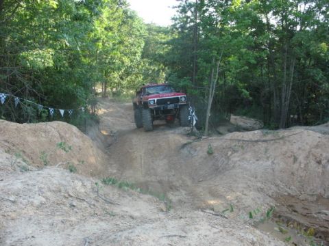 1979 Ford Bronco - A modified red SUV navigates a challenging dirt track in an off-road park.