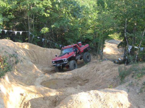 1979 Ford Bronco - A modified red Ford F-150 navigates a challenging off-road course with steep inclines and muddy puddles.