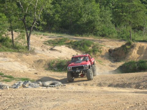 1979 Ford Bronco - A modified red truck navigates a challenging off-road course with dusty terrain.