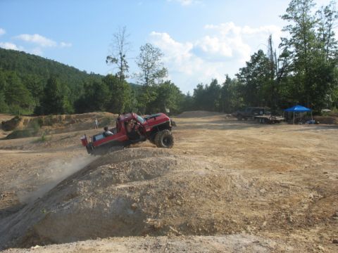 1979 Ford Bronco - A red off-road truck navigates a steep dirt incline at an off-road park, with another vehicle and trailer visible in the distance.
