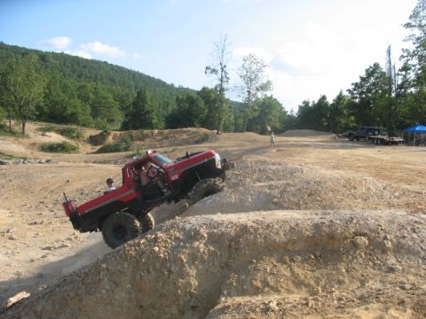 1979 Ford Bronco - A red off-road truck navigates a steep dirt incline at an off-road park, with other vehicles visible in the distance.