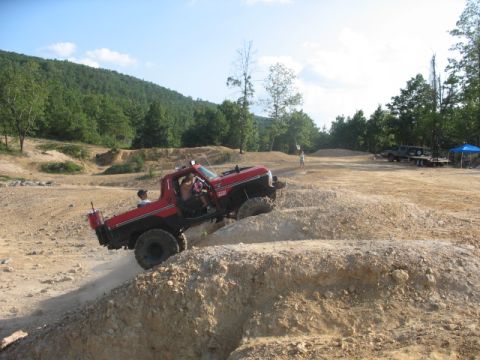 1979 Ford Bronco - Off-road pickup truck navigates a steep dirt incline at a park, with other vehicles and trees in the background.
