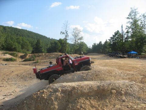 1979 Ford Bronco - A red pickup truck navigates a challenging dirt terrain at an off-road park.