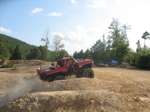 1979 Ford Bronco - A modified red truck navigates a challenging off-road course under a partly cloudy sky.