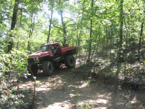 1979 Ford Bronco - A modified red pickup truck navigates a steep, wooded trail during an off-road excursion.