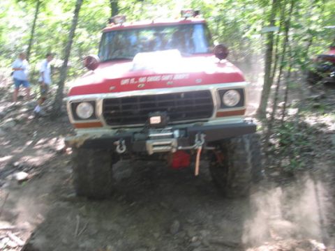 1979 Ford Bronco - A red 1979 Ford Bronco navigates a dusty off-road trail with trees on either side.