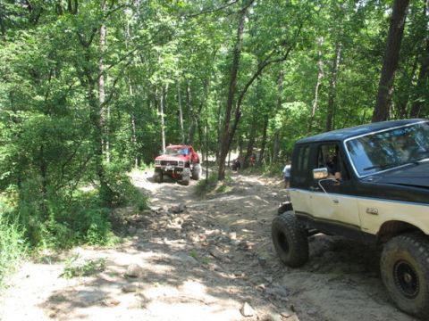 1979 Ford Bronco - Off-road vehicles navigate a challenging dirt trail in a wooded area.