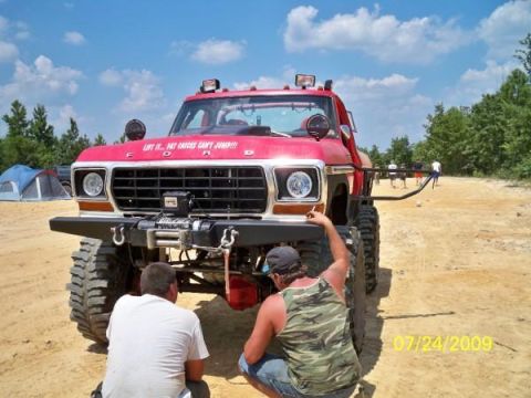 1979 Ford Bronco - A modified red Ford pickup truck is the focus of this off-road park scene on a sunny day.
