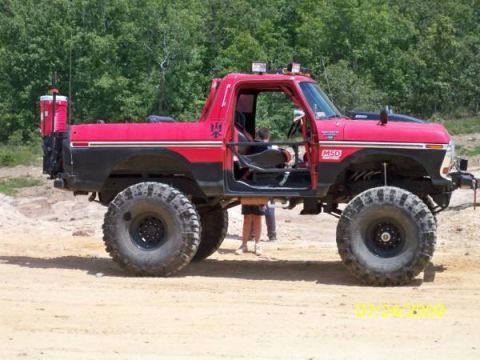 1979 Ford Bronco - Modified red truck with oversized tires and off-road modifications sits on a dirt surface.