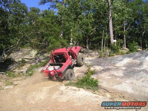 1979 Ford Bronco - Off-road vehicle navigates a challenging rocky trail in a wooded area.