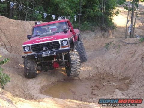 1979 Ford Bronco - This heavily modified red Ford truck tackles a challenging off-road trail with large tires and a lifted suspension.