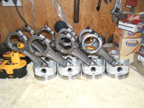 1988 Ford Bronco - Engine pistons and connecting rods are laid out on a workbench, with tools and boxes in the background.