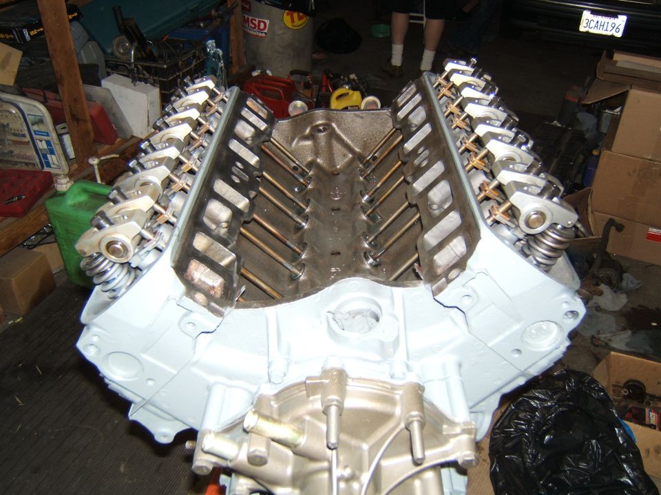 V8 engine block with rocker arms and valve springs visible. Light blue paint on the block