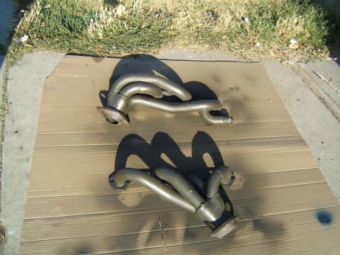 1988 Ford Bronco - A pair of exhaust headers are laid out on a piece of cardboard on a sunny day.