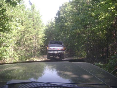 1990 Ford Bronco - A 1990 Ford Bronco drives down a wooded dirt road, seen from another vehicle.