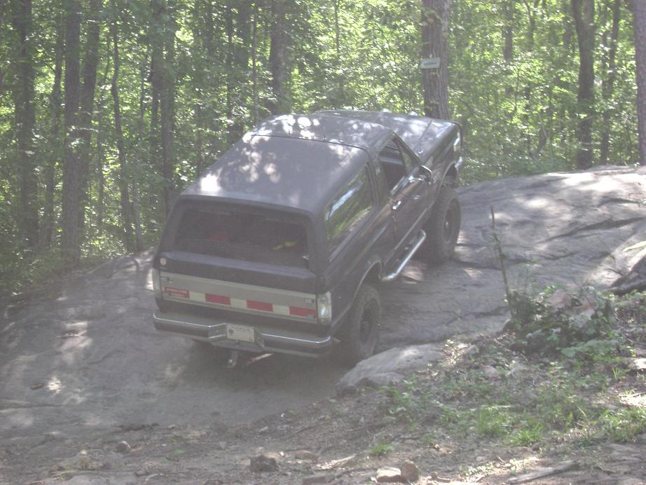 1990 Ford Bronco on a dirt and rock trail in a wooded area