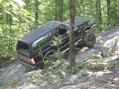 1990 Ford Bronco - This SUV is navigating a challenging rocky terrain in a forest setting.