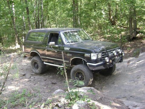 1990 Ford Bronco - A black Ford Bronco navigates a rocky, wooded trail.