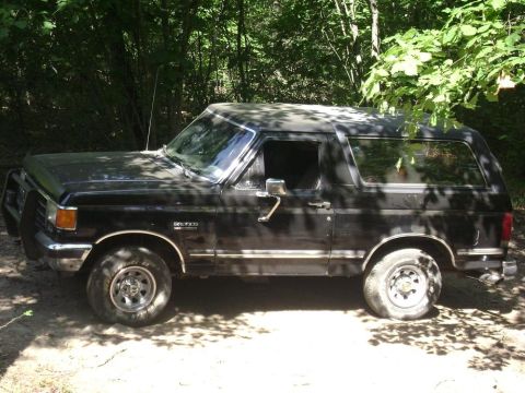 1990 Ford Bronco - This 1990 Ford Bronco is seen from the side, parked amongst trees, a front brush guard.